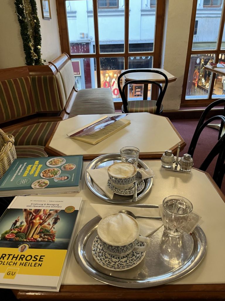 Im 1. Stock im Café Heiner mit Blick auf die Wollzeile, im Vordergrund 2 Melange und die neuen Bücher: Arthose endlich heilen und das neue Buch von Bettina Matthaei und Daniela Kielkowski „Abnehmen mit Kohlenhydraten“