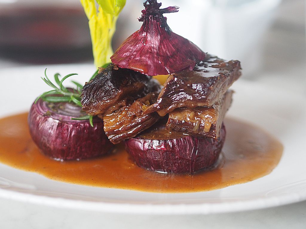 Geschmortes Beinfleisch mit gebratenen roten Zwiebeln mit Polenta auf dem Teller