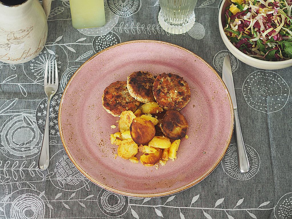 Faschierte Lachs-Kabeljaulaberln mit Bratkartoffeln und Chicorée-Radicchio-Salat auf dem Tisch