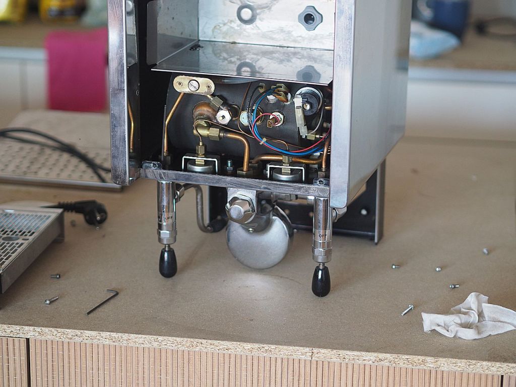 Innensicht einer Kaffeemaschine mit sichtbaren Rohrleitungen und elektronischen Komponenten auf einem Tisch.