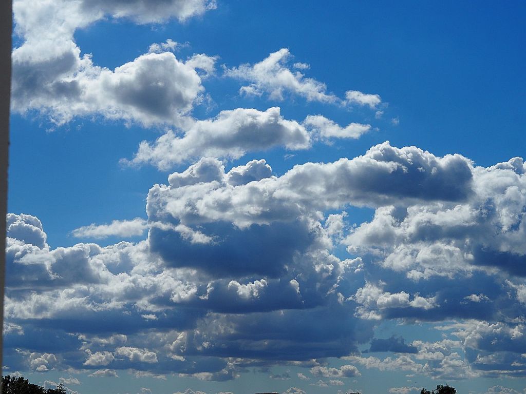 Ein blauer Himmel mit vielen weißen, fluffigen Wolken, die über den Horizont ziehen.