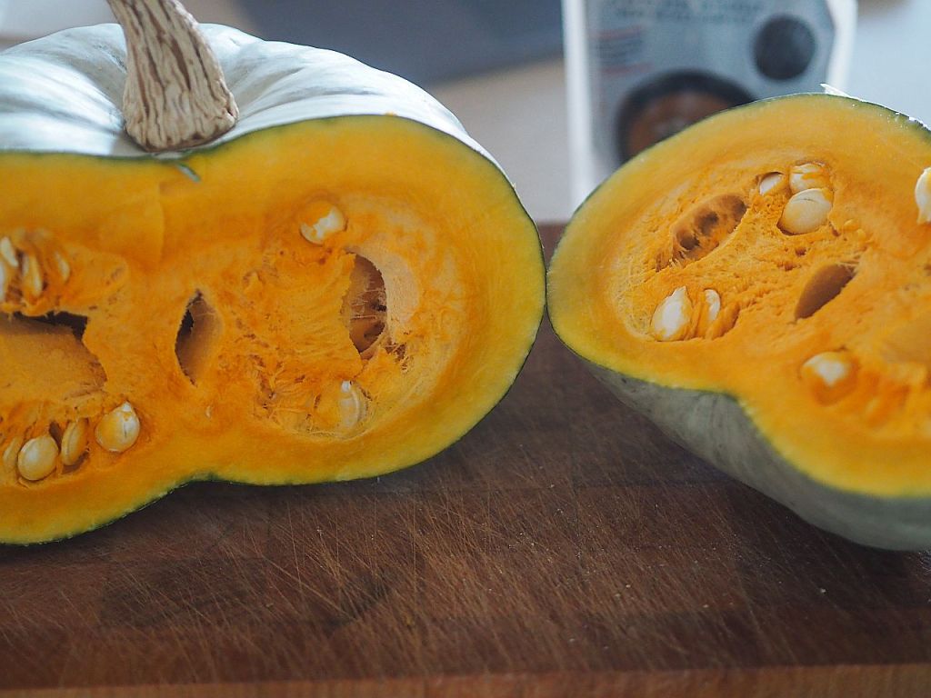 Ein aufgeschnittener Kürbis auf einem Holzbrett, der orangefarbenes Fruchtfleisch und Kerne zeigt.