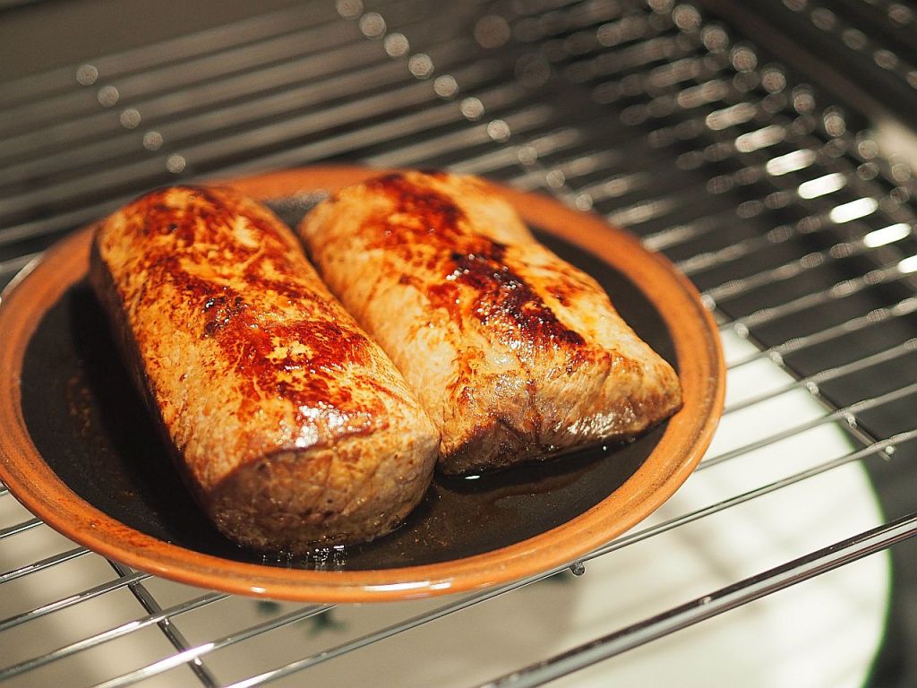 Zwei perfekt gegrillte Fleischstücke auf einem braunen Teller, der auf einem Rost im Ofen steht.
