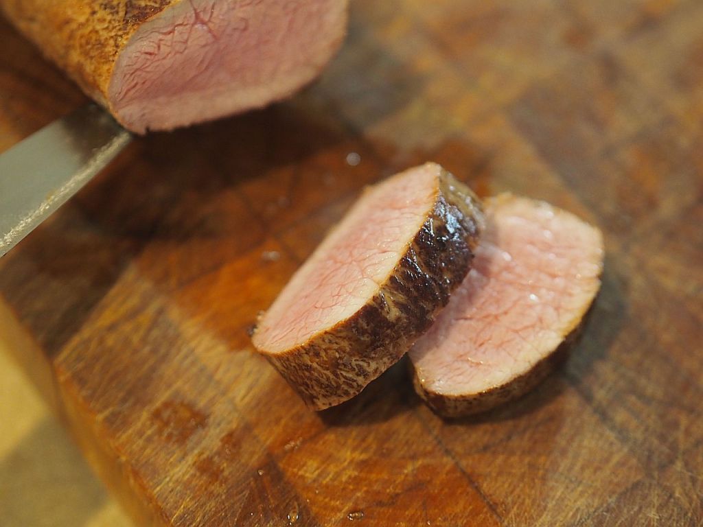 Ein Stück Rinderfilet, das in Scheiben geschnitten und auf einem Holzbrett präsentiert wird. Die Schnitte zeigen eine zarte, rosa Innenseite.