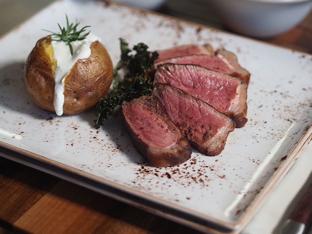 Ein Teller mit saftigem Rindersteak, das in Scheiben geschnitten ist, serviert mit einer Ofenkartoffel, die mit Sauerrahm und frischem Dill garniert ist, sowie gebratenem Grünkohl.