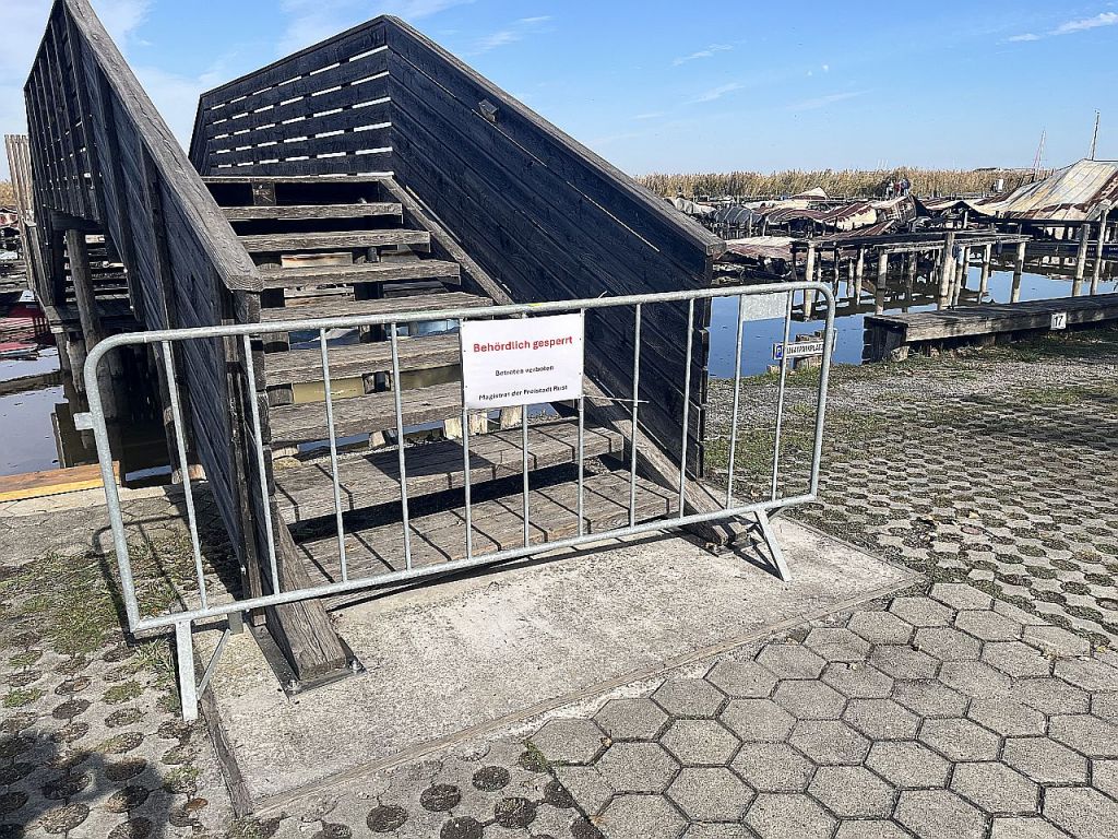 Abgesperrte Holztreppe zu einem Steg mit einem Hinweisschild, das auf eine behördliche Sperrung hinweist.