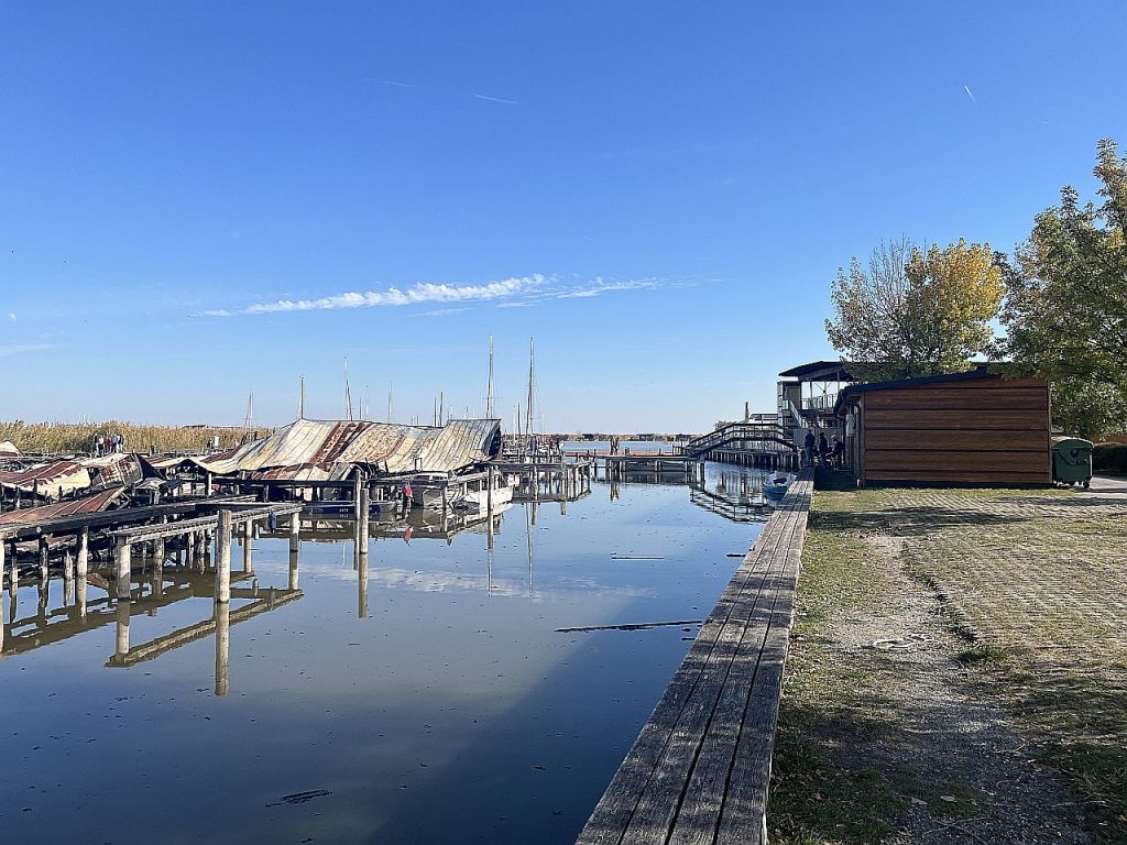 Ein ruhiger Hafen mit Booten, Holzstegen und reflektierendem Wasser bei klarem, blauem Himmel.