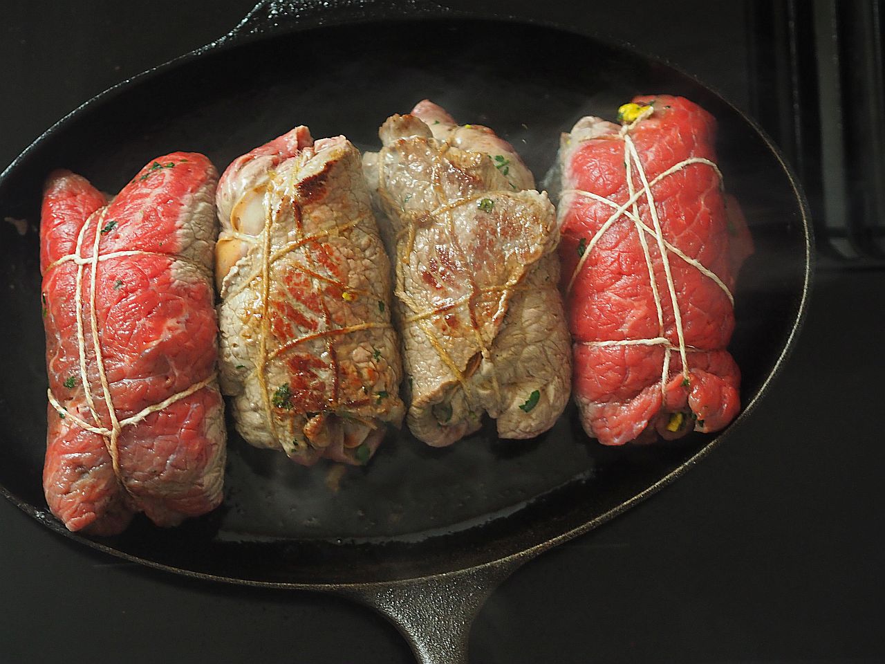 Eine Pfanne mit mehreren Rinderrouladen, die in Küchengarn gebunden sind, während sie braten.