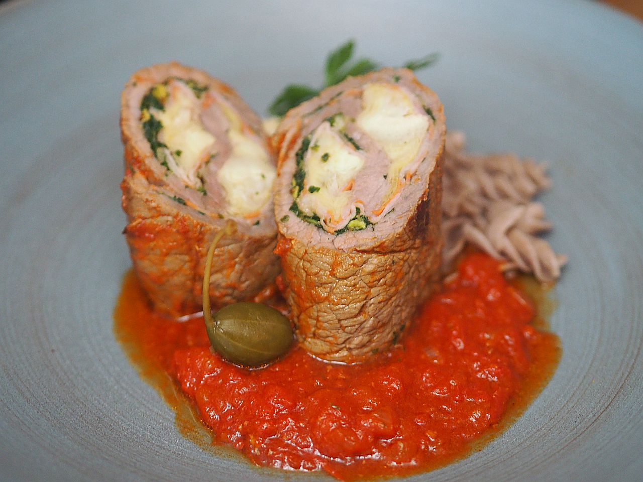 Aufschnittrolle mit einer Füllung aus Käse und Kräutern, serviert auf einer Tomatensauce.