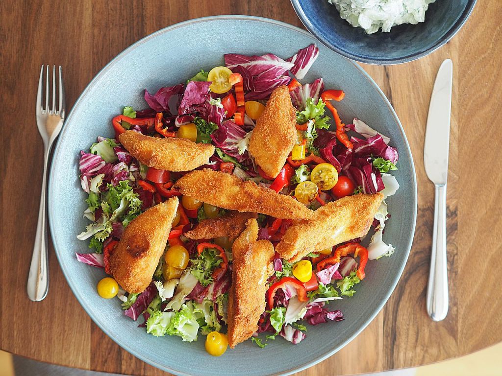 Ein bunter Salat mit knackigem Gemüse, überzogen mit knusprigen Panade-Streifen, serviert in einer großen flachen Schüssel.